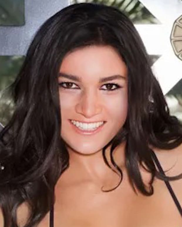 Michelle Jenneke poses in a dark purple string bikini in front of a wooden and glass-paneled wall.